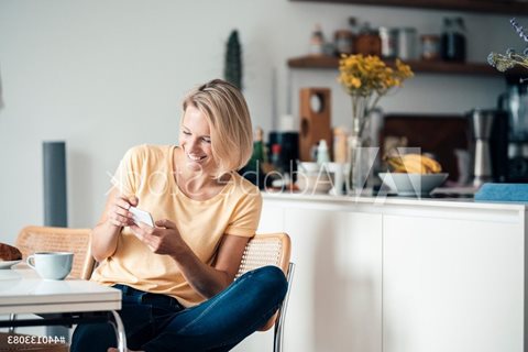 a woman sitting at a table in a kitchen looking at her phone